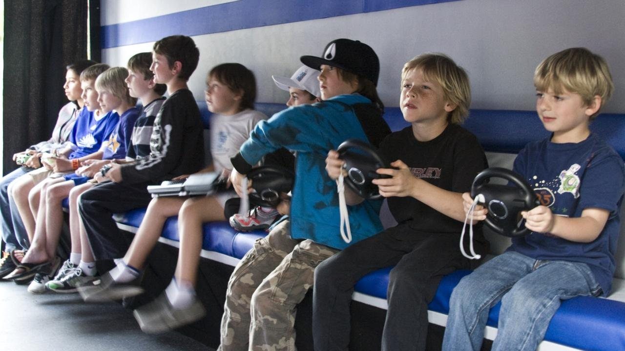 Children sitting side by side playing video games together inside a mobile game truck
