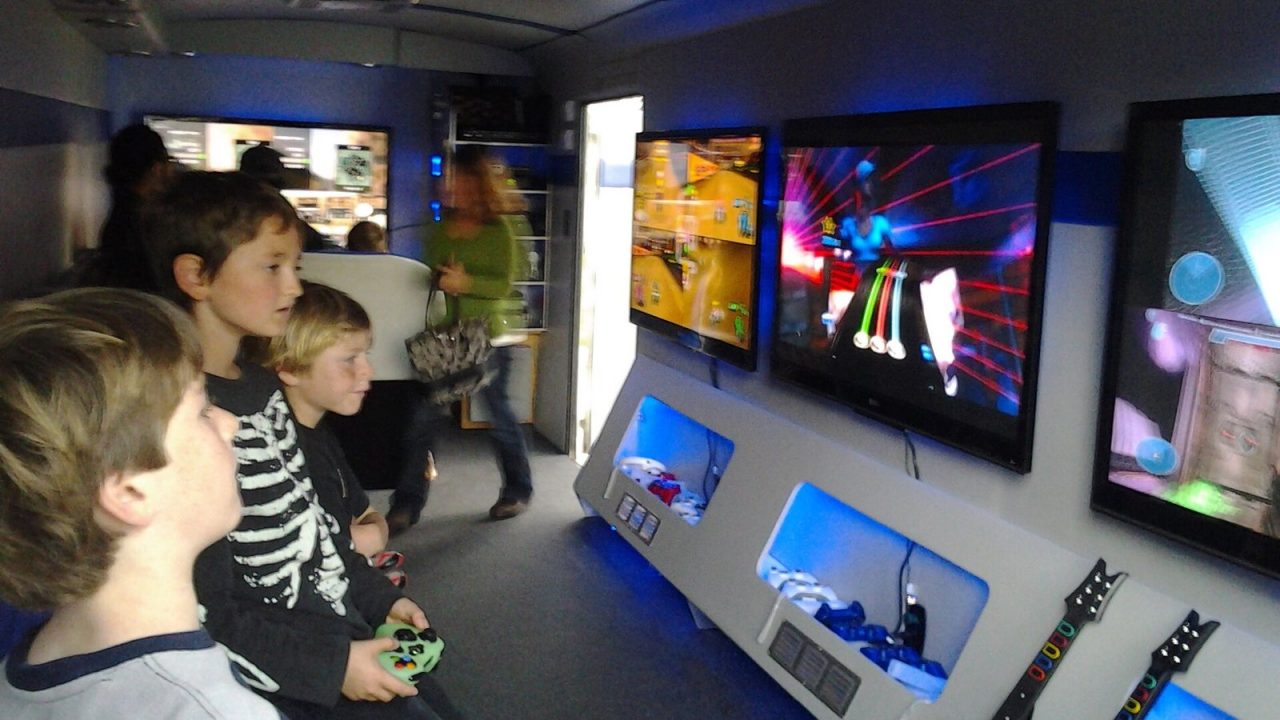Children playing video games together in front of a row of TV screens