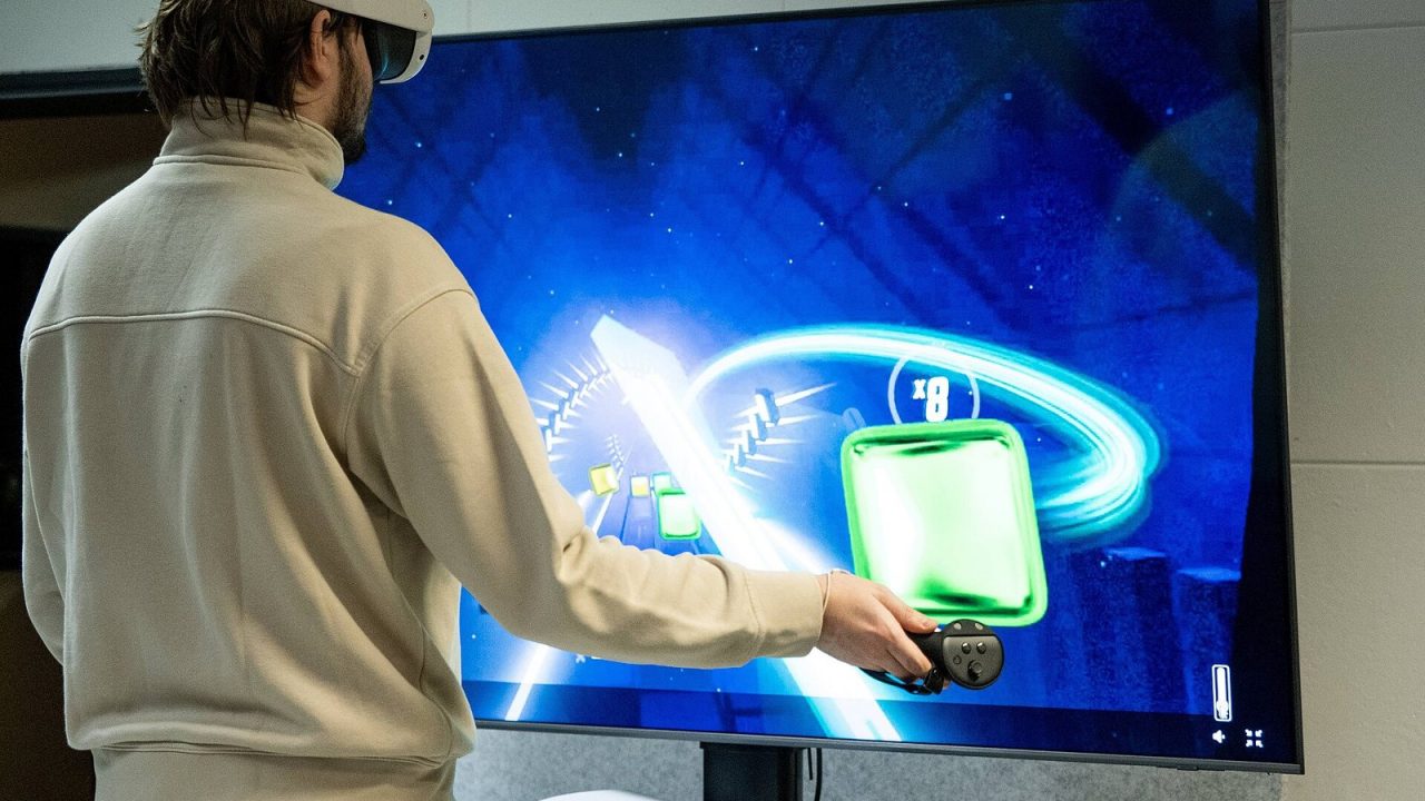 Young man in a VR headset holding a controller and standing in front of a large projection screen
