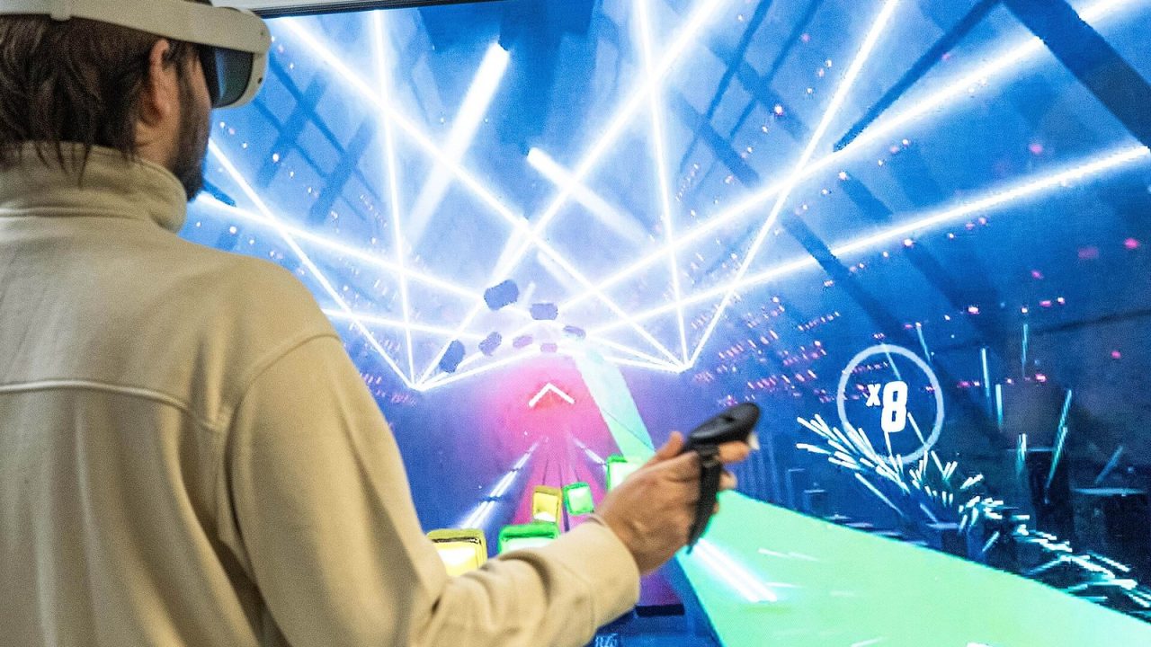 Young man wearing a VR headset and holding a motion controller while standing in front of a large screen